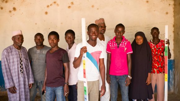 A group of female and male community volunteers stand for a portrait holding dose poles.