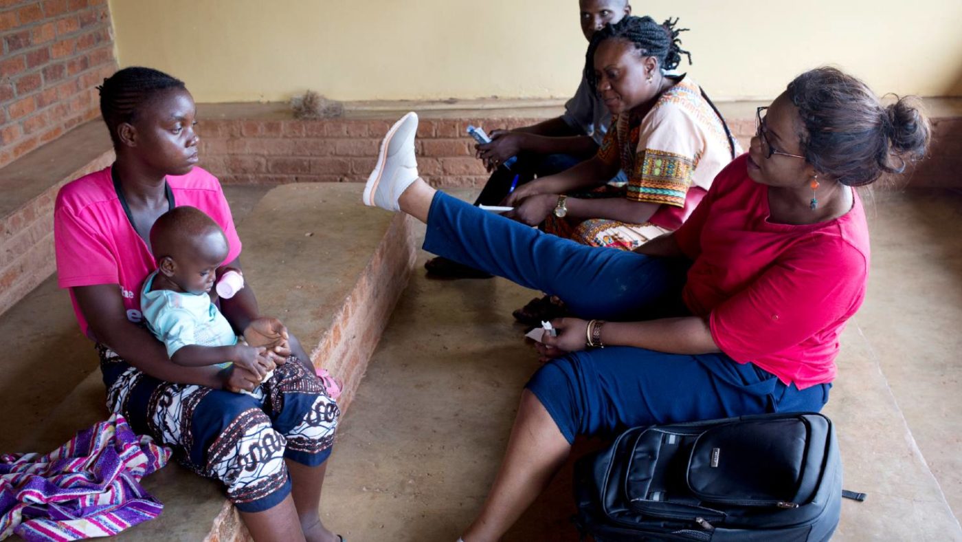 A doctor shows a patient who has lymphatic filariasis how to reduce swelling by putting her leg up.