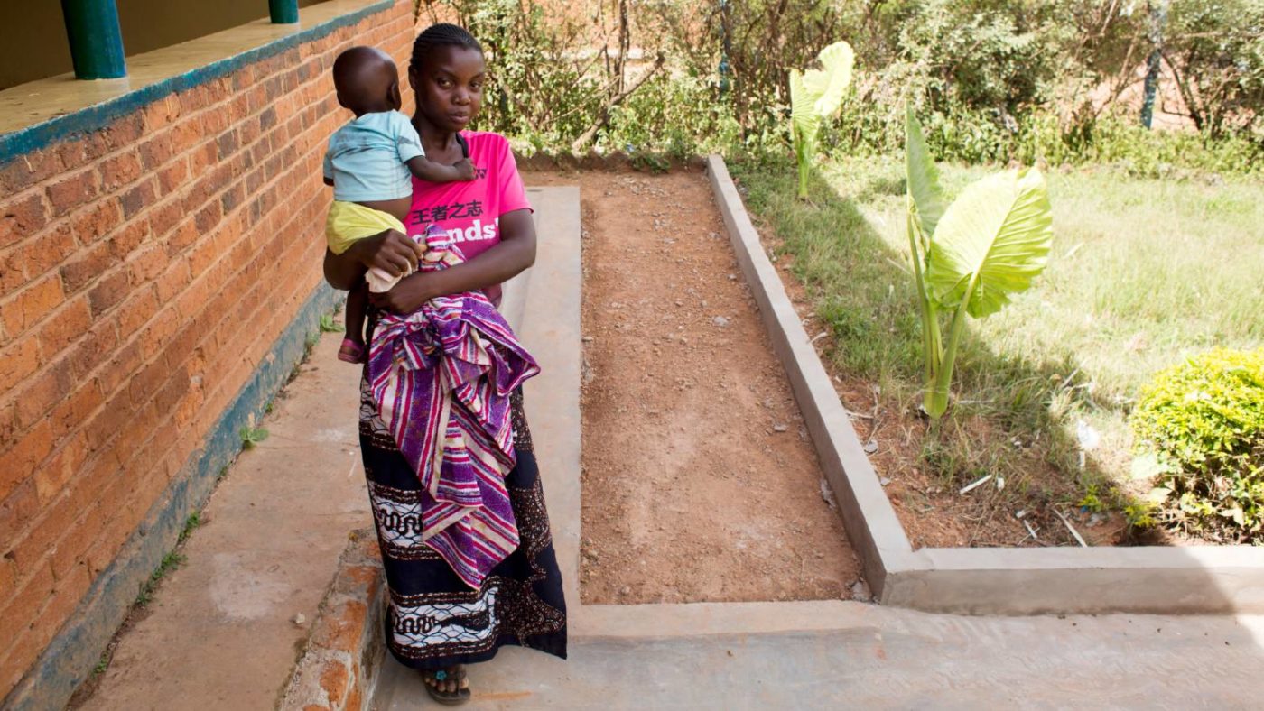 A woman holding her baby stands outside a clinic.
