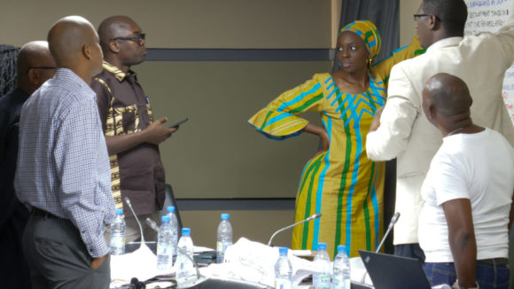A woman gives a talk to a group of men.