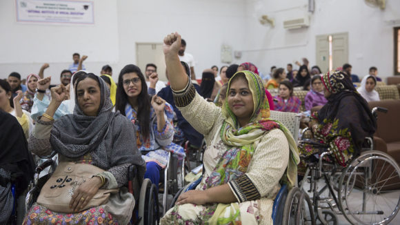 A group of people with disabilities raise their hands.