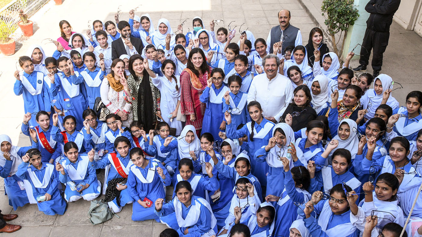 A large group of children stand with the the minister of education. They are smiling and many are holding glasses.