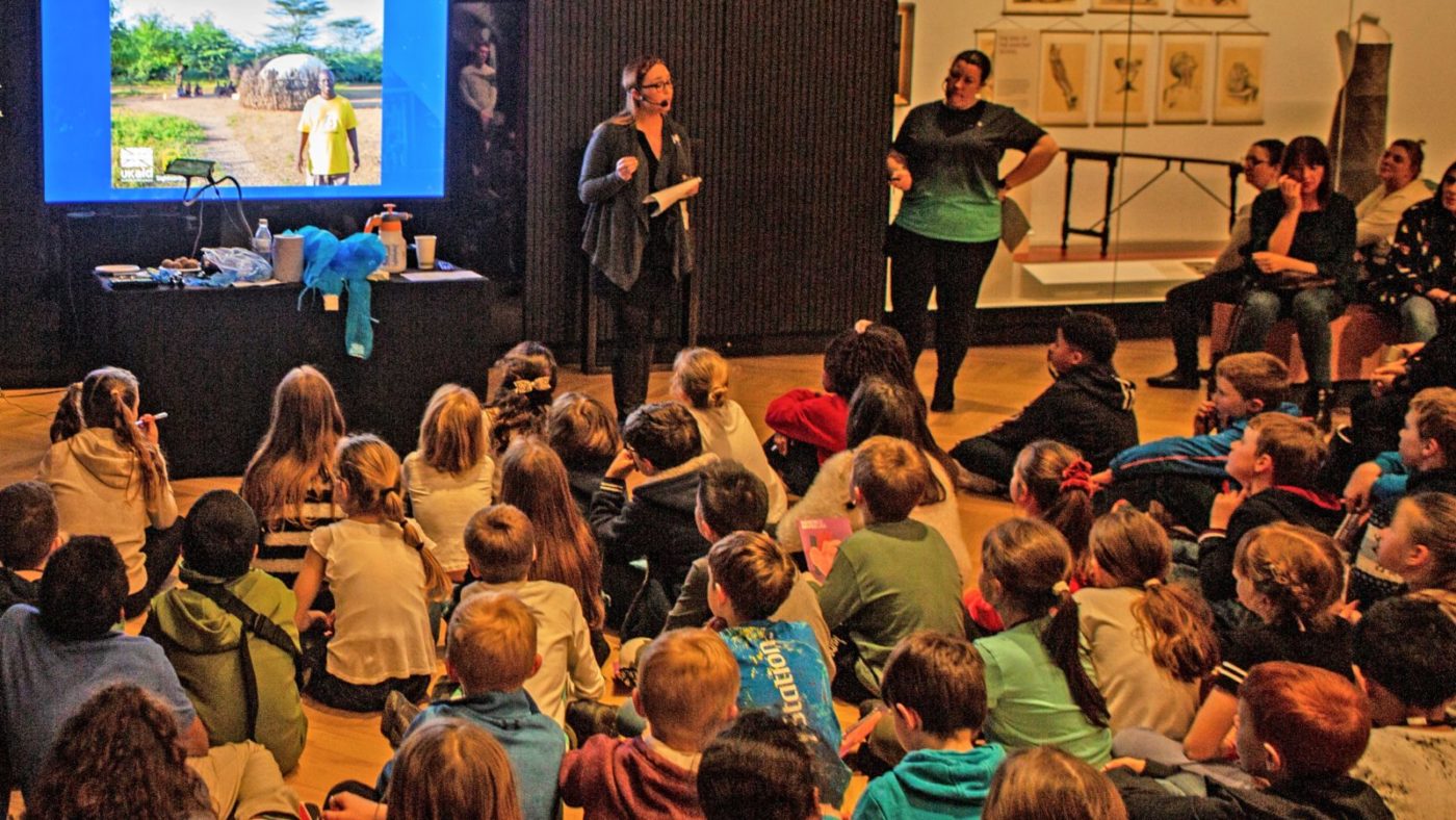 A group of children sit on the floor at the museum listening to a talk by Sightsavers