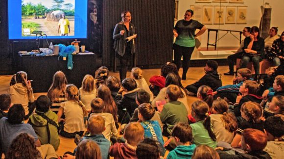 A group of children sit on the floor at the museum listening to a talk by Sightsavers