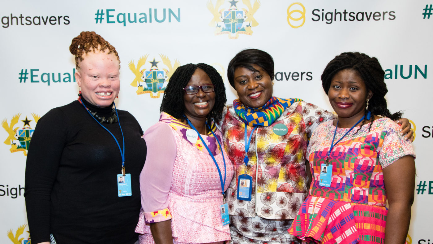 Four women standing together smiling, in front of a backdrop that says #EqualUN.