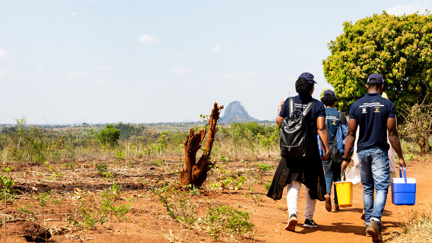 A group of people walking along a remote road. They are carrying buckets and coolers.