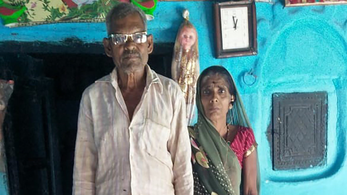 A husband and wife stand outside their home.