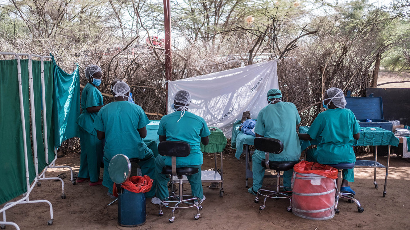 A group of surgeons perform an operation outside under a tree.
