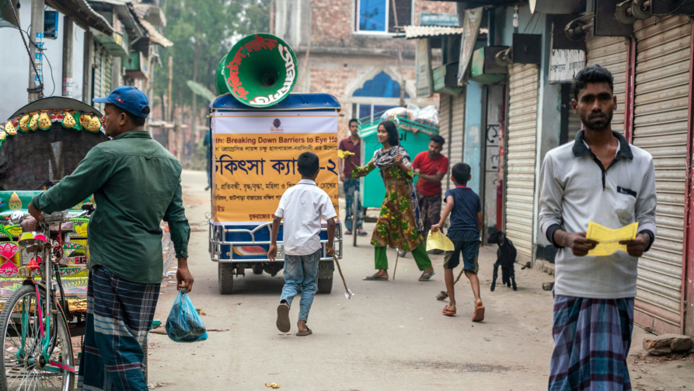 A miking tuk-tuk passes through a busy street.