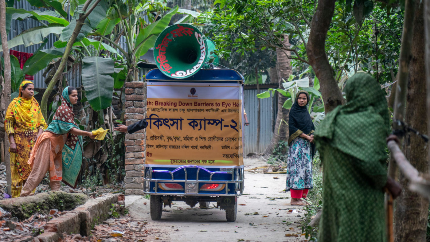 A tuk tuk passes a group of women.