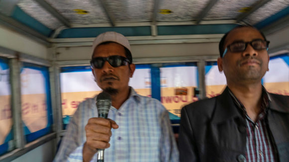 Two men announcing messages into a microphone in a tuk-tuk.