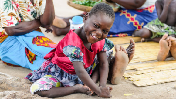 A young girl sitting on the ground outside.