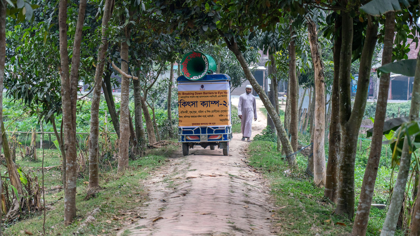 A miking tuk-tuk driving through a street in Bangladesh.