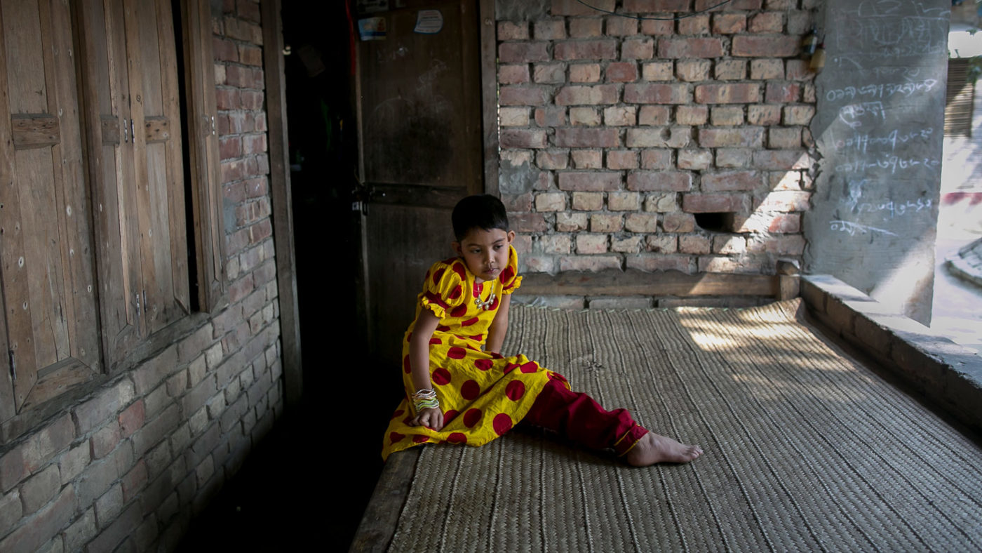 Muslima, an eight-year-old girl, sitting in the dark outside her home and looking at the floor.