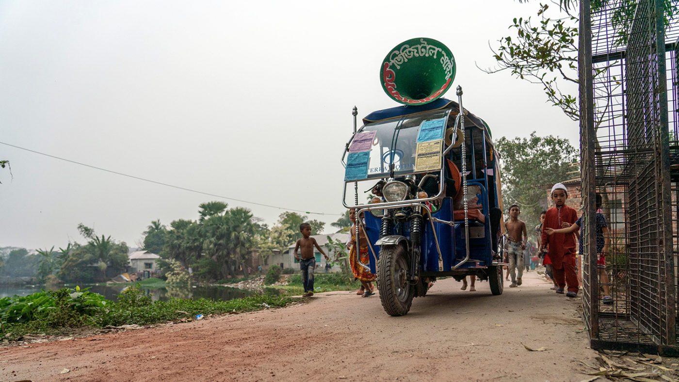 A miking tuk-tuk driving through a street in Bangladesh.