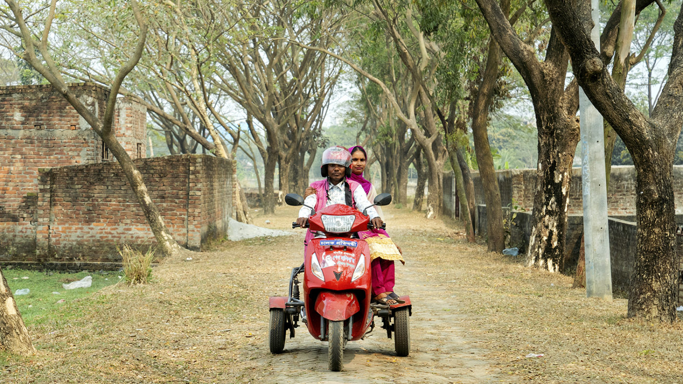 A man and woman riding a motorbike along a rural road.