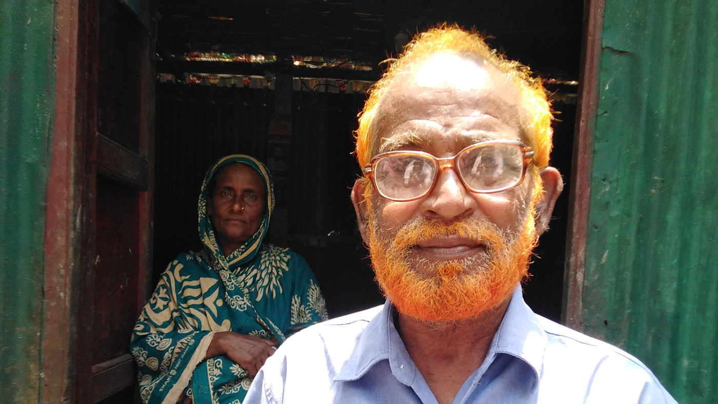 A man stands in front of his home. His wife stands in the doorway.