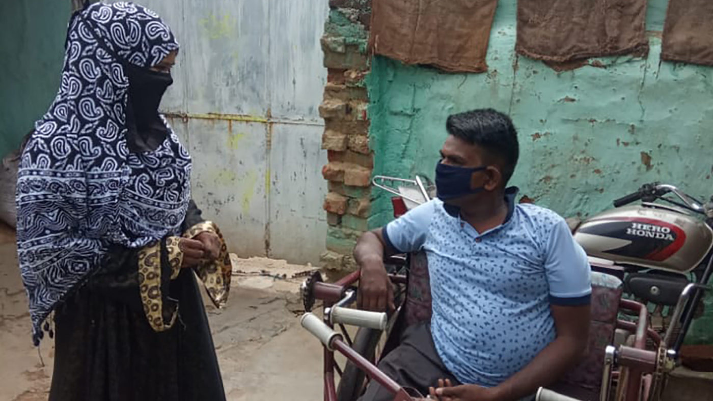A lady wearing a face covering speaks to a man in a wheelchair.