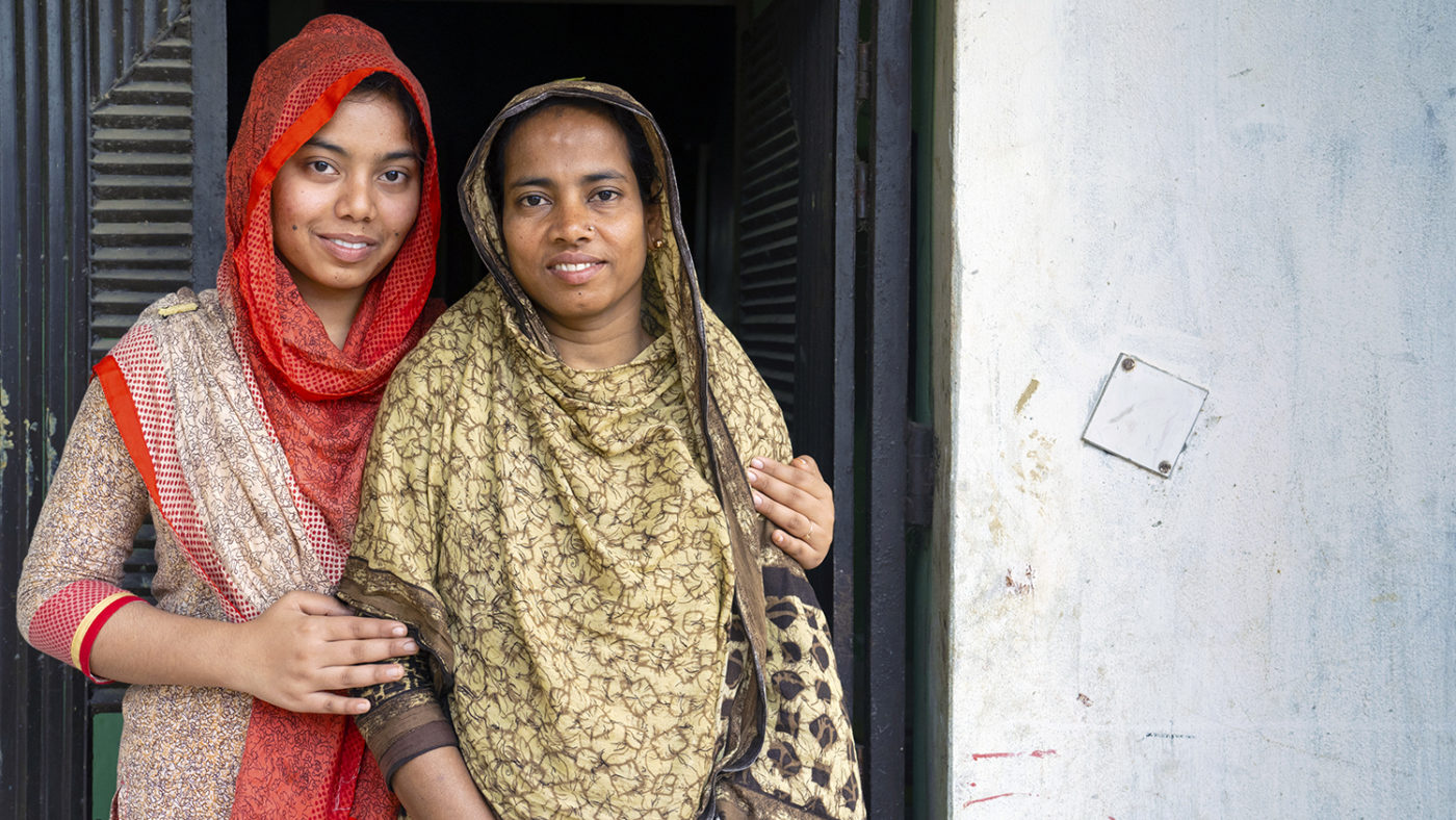 A teenager and her mother stand together smiling.