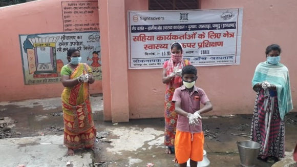 A group of four people stand outside wearing protective masks and washing their hands.