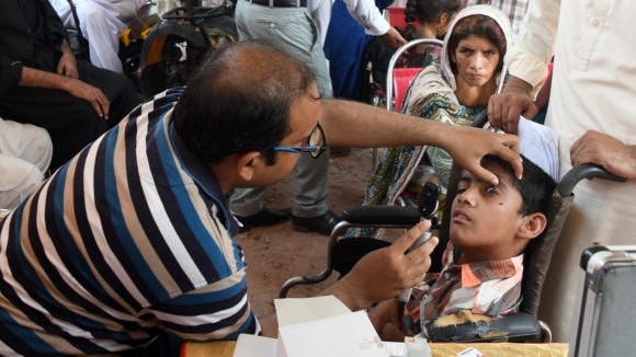 A man examines the eyesight of a young boy who uses a wheelchair.