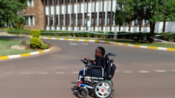 A young man using a wheelchair on a road in Kenya.