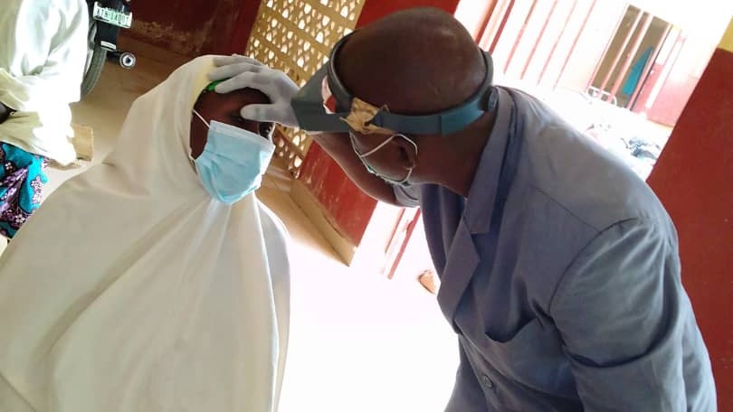 Kabir examines a lady's eye. Both people wear face masks