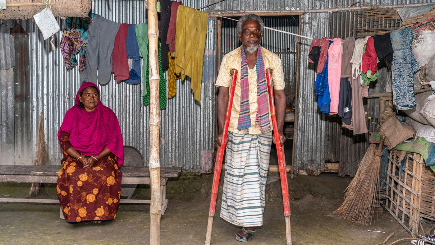 A woman sitting and a man using crutches to stand.