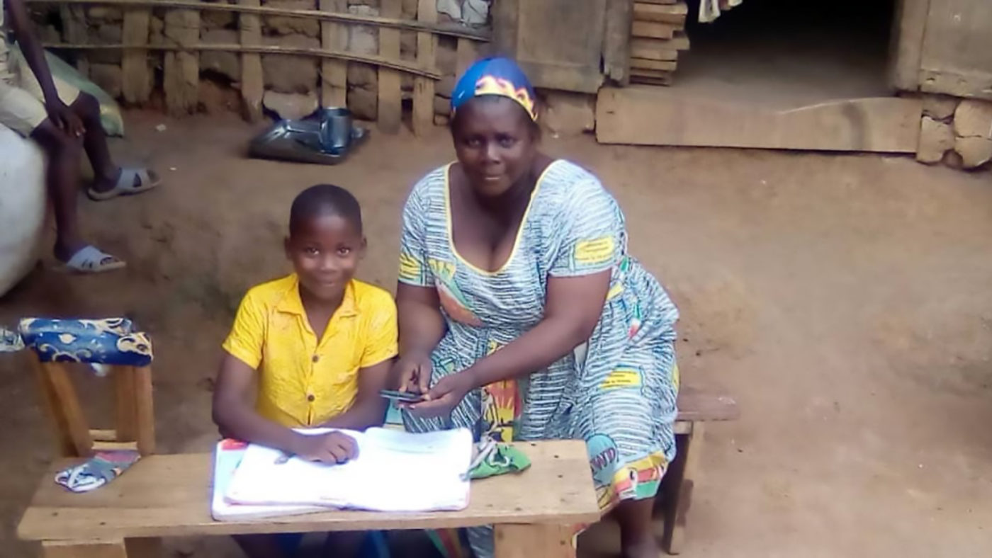A boy sits outside his house with his mother who is helping him fill in school work.