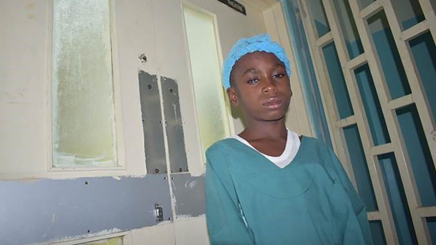 A boy wearing a hospital cap and gown waits outside the operating theatre.
