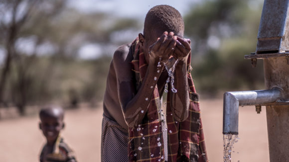 A boy washes his face at a well.