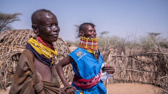 Two people in traditional clothing stand outside in remote Turkana, Kenya.
