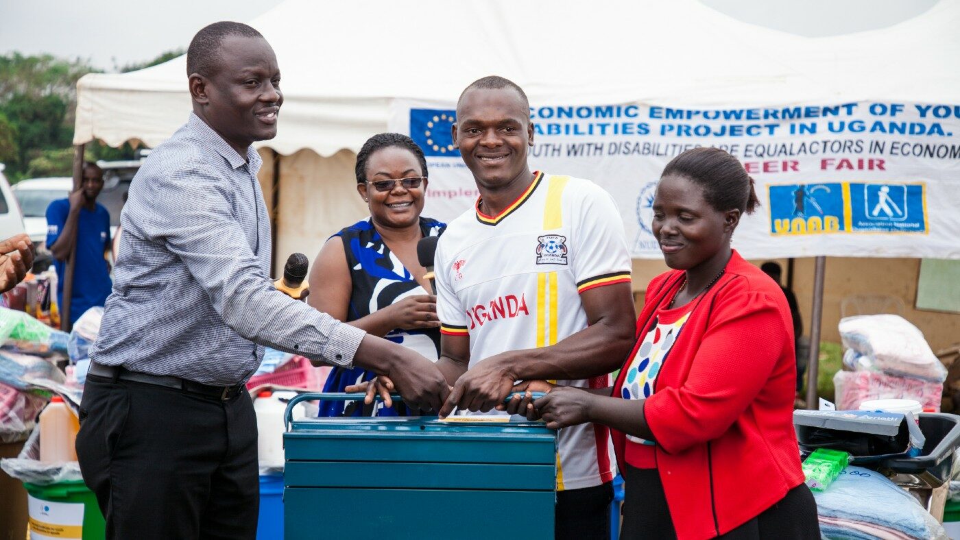 A Masindi district official and the Sightsavers programme manager hand over a motor repair tool kit to Sharif at the careers fair.