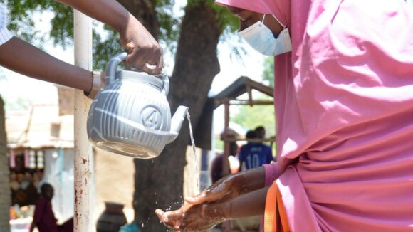 A volunteer drug distributor washing hands washes someone's hands.