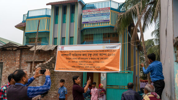 Men putting up a sign to welcome people in Rangpur, Bangladesh to a free eye screening camp.