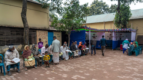 Men sit outside waiting for an eye test.