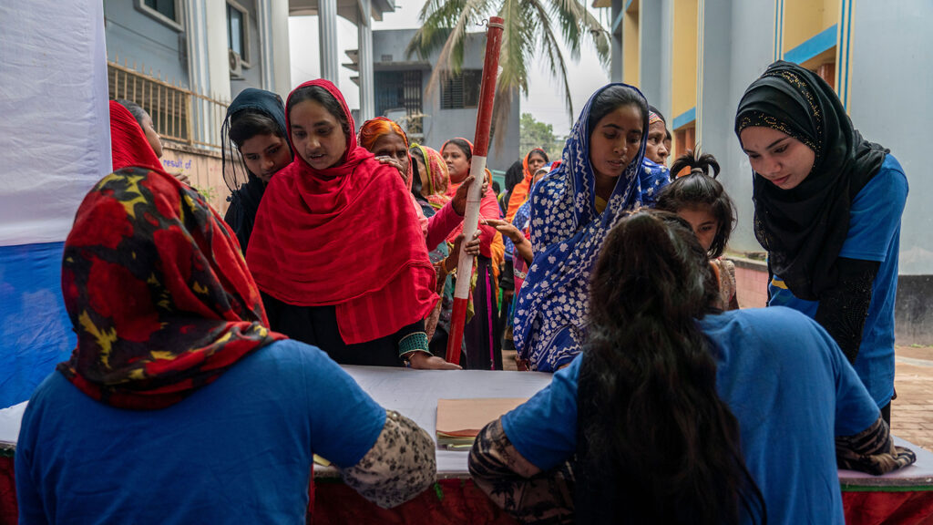 Two women sit on a registration desk with a queue of people waiting.