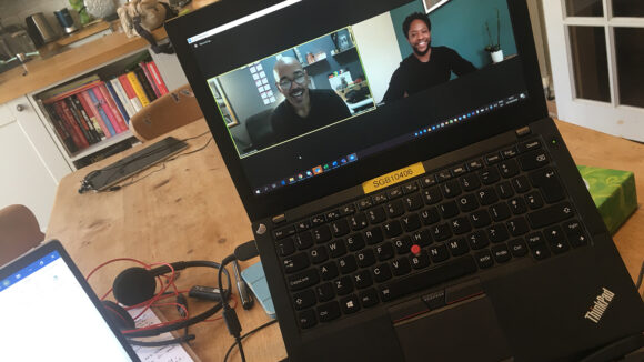 A workstation is set up in someone's kitchen. On the screen there are two men having a video call.