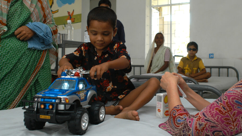 A boy sitting on a hospital bed, playing with a toy truck.