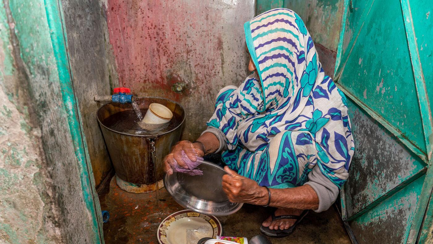 A woman sits on the ground washing dishes.