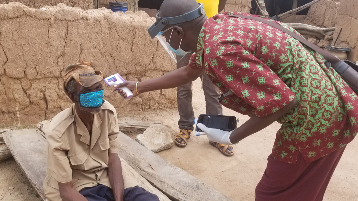 A volunteer wearing a visor and mask checks a person's temperature.