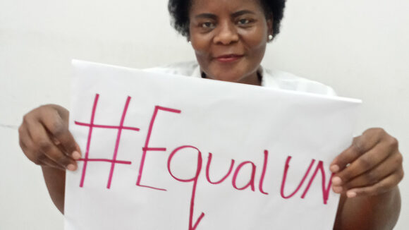Eufémia Amela smiles and holds a sign saying #EqualUN.