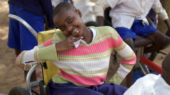 A girl in a wheelchair smiles to camera.