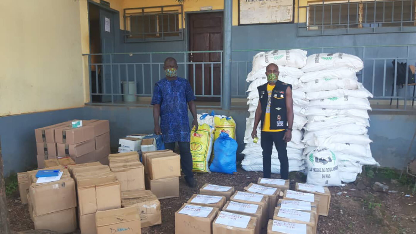 Two men stand outside with many parcels of medication.