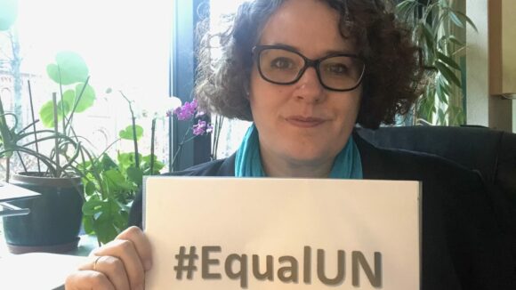 A woman holds a sign saying #EqualUN.