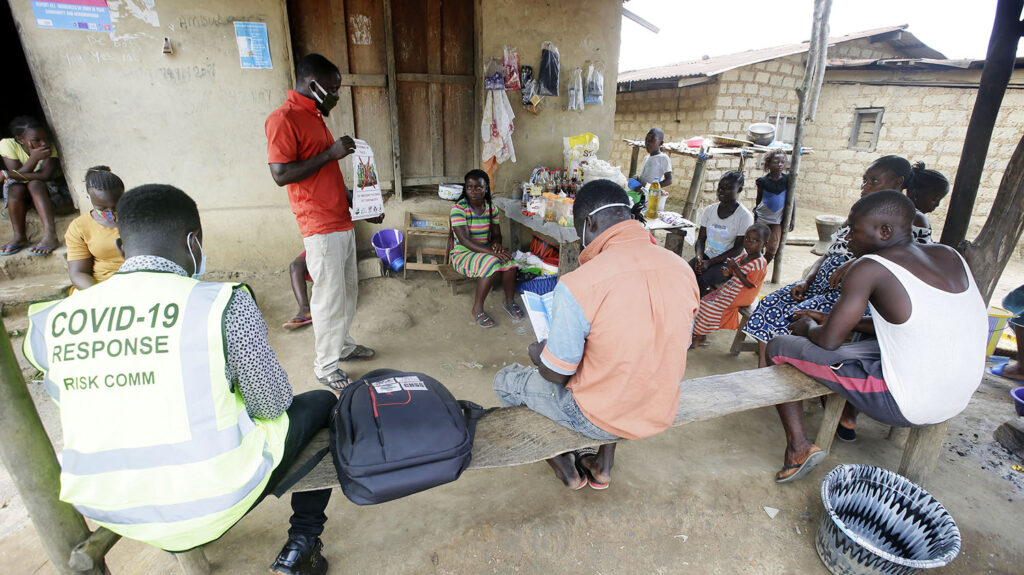 A man holds up a poster to community members during a COVID awareness campaign.