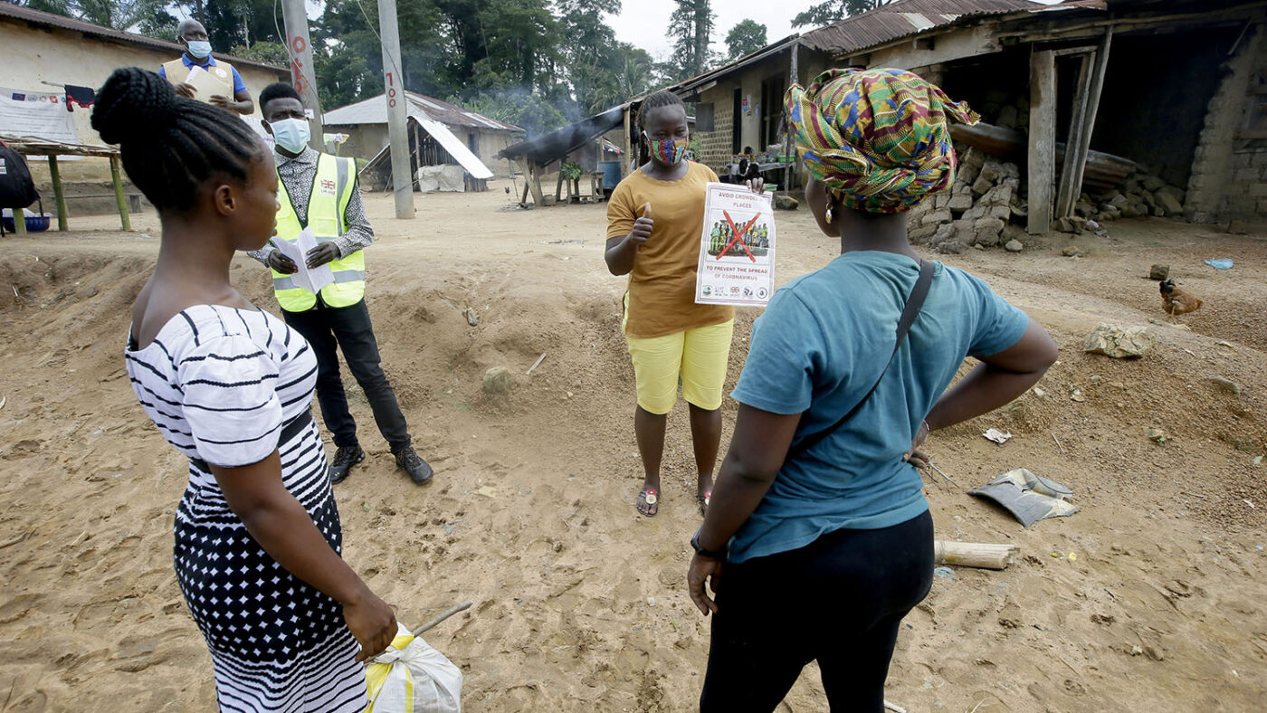 A woman holds up a poster and shares information with two other women.