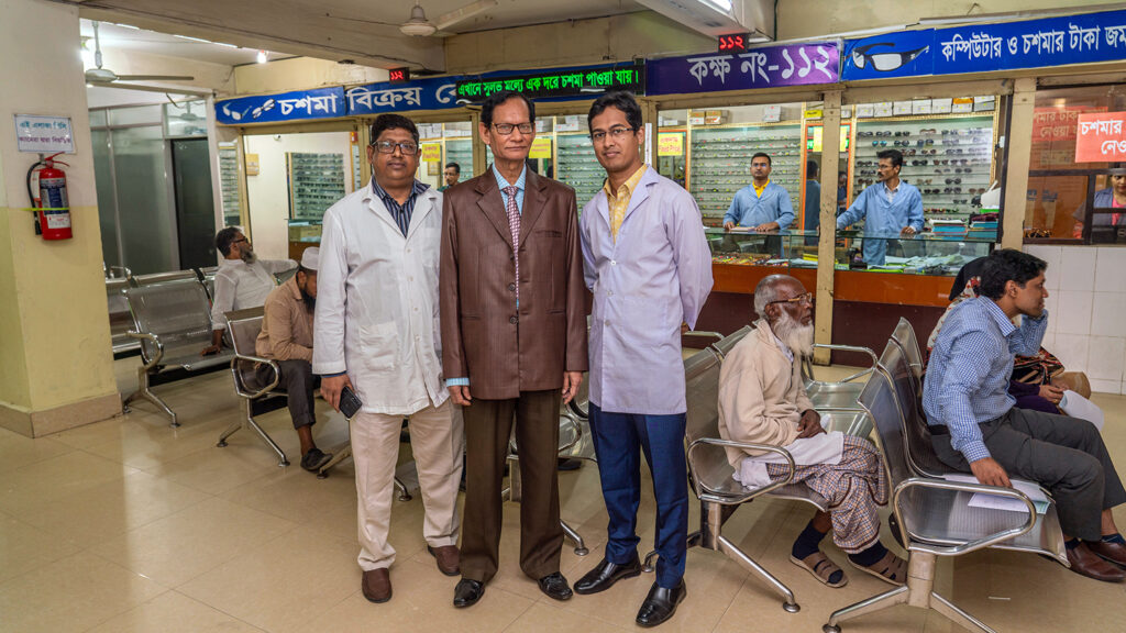 Three men stand in a waiting room in a hospital.