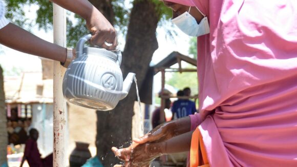Woman wearing face mask washing hands from a kettle