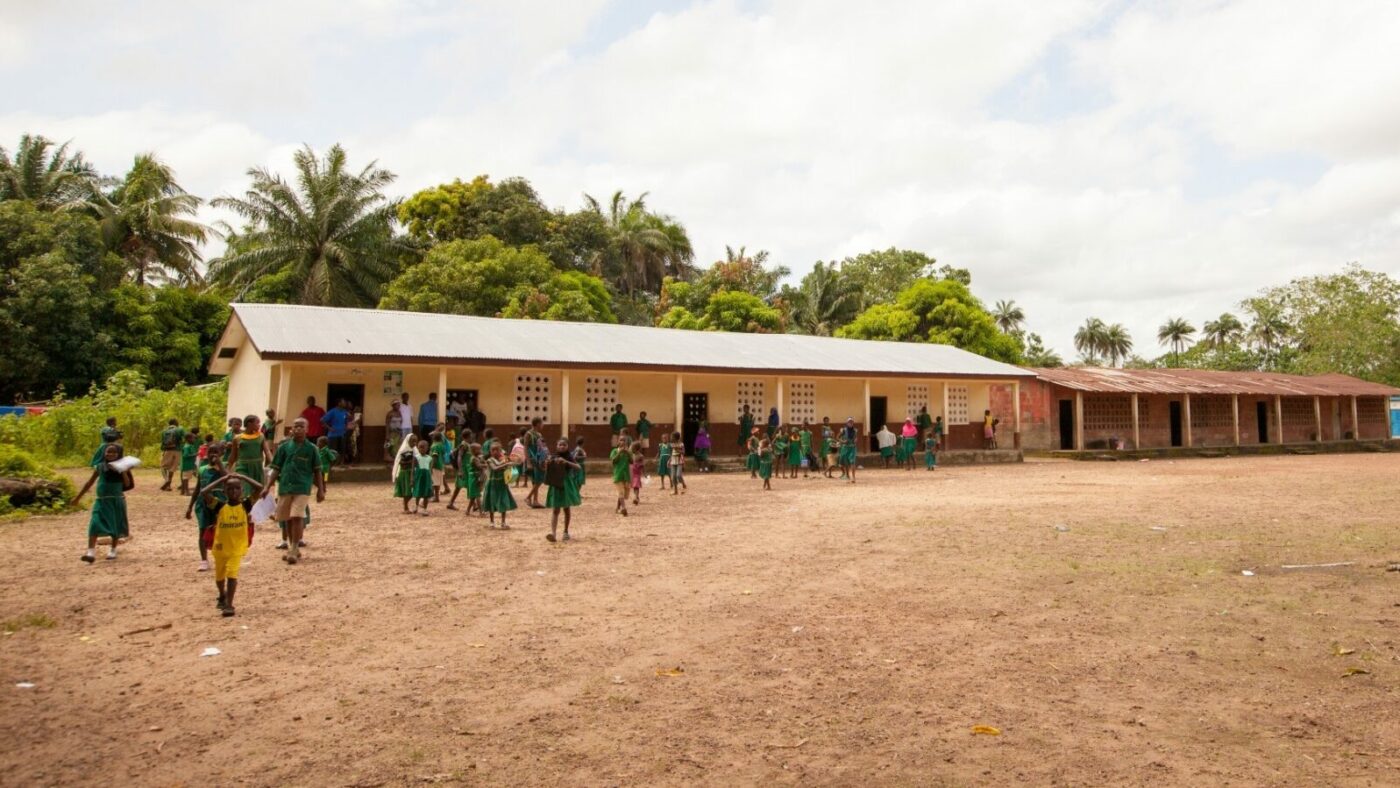Children play on a playing field in front of a long, low school building